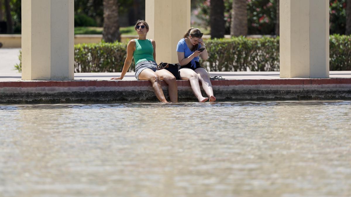 Dos personas se refrescan en una fuente de los jardines del antiguo cauce del Turia para combatir el calor que vive durante este lunes..
