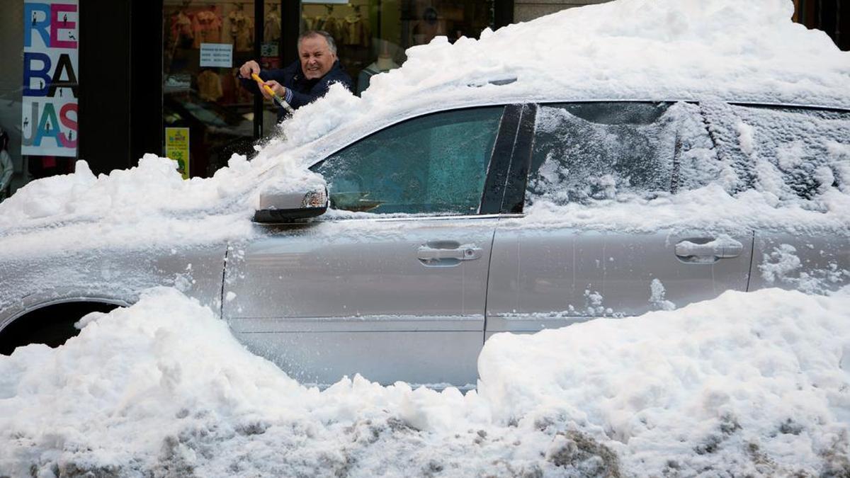 Un hombre limpia de nieve su coche atrapado por la nieve en una céntrica calle de Ávila.