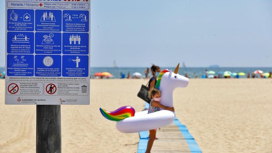 Una niña con mascarilla carga su flotador hacia la orilla de la playa de Las Arenas, en Valencia.