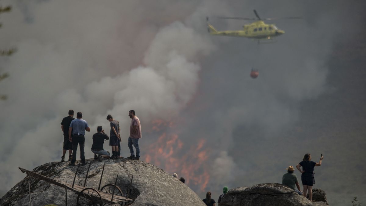 Varias personas observan la labor de un helicóptero de extinción del incendio forestal declarado en Avión (Ourense) este lunes.