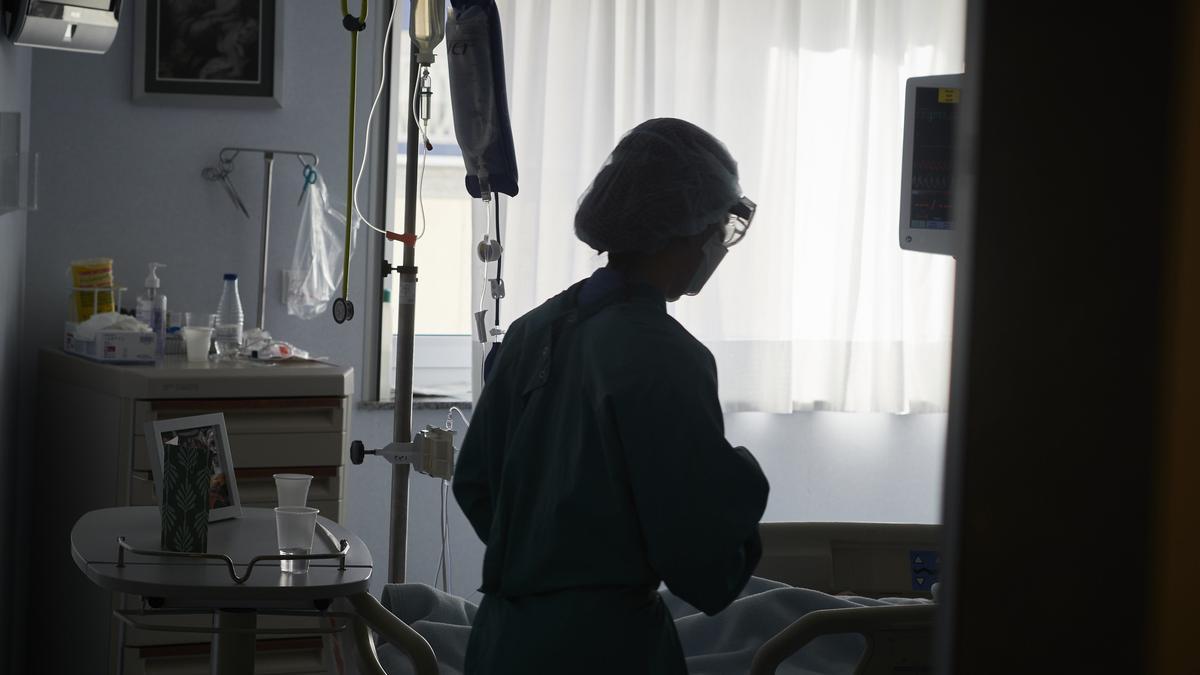 Un trabajador sanitario atiende a un paciente en una camilla de la UCI.