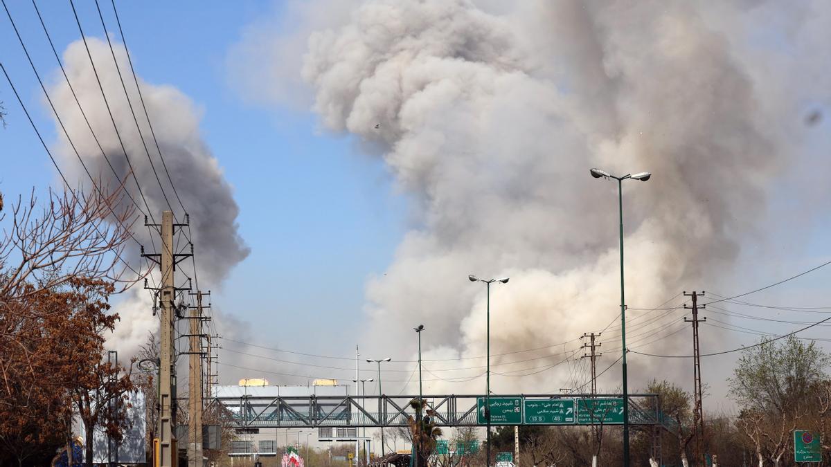 La gente corre en busca de refugio mientras el humo se eleva tras un ataque aéreo en el centro de Teherán, Irán.