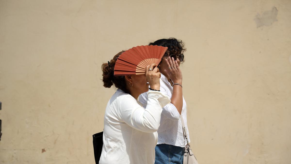Varias personas se protegen del sol en una calle de Málaga. A 27 de junio de 2025, en Málaga (Andalucía, España).