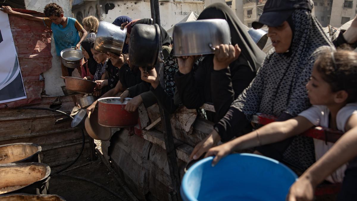 Palestinos, incluidos niños, sostienen ollas mientras hacen fila para recibir comida.