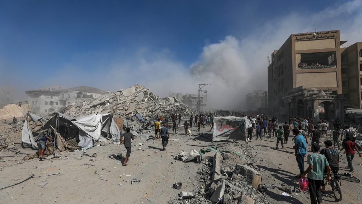 Los palestinos caminan entre escombros mientras el humo se eleva desde el edificio residencial Al-Roya tras un ataque aéreo israelí en el oeste de la Ciudad de Gaza.
