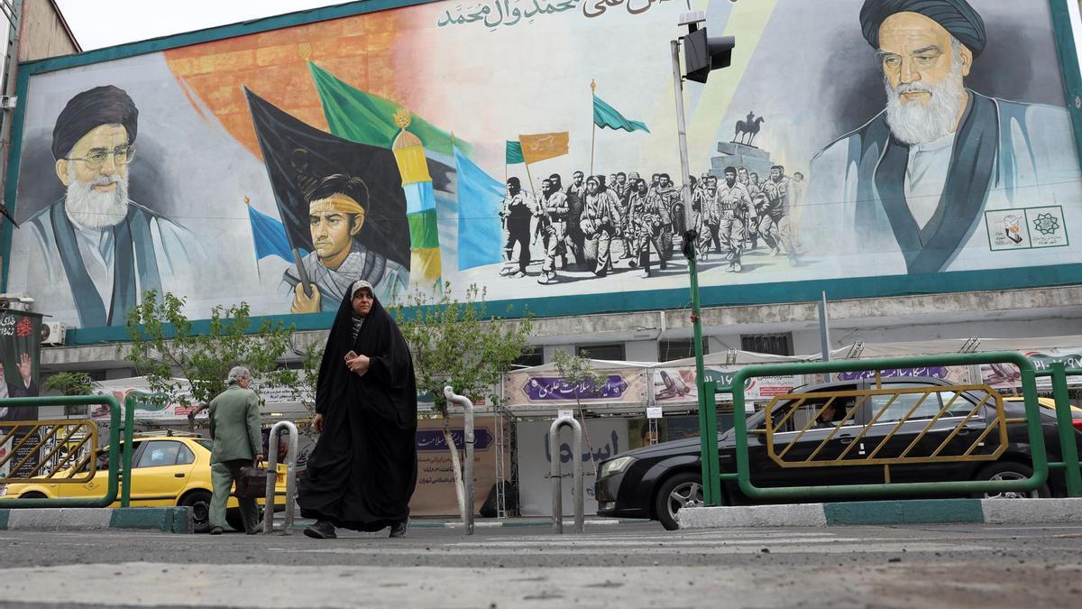 Una mujer camina junto a una valla publicitaria que representa a los líderes supremos iraníes
