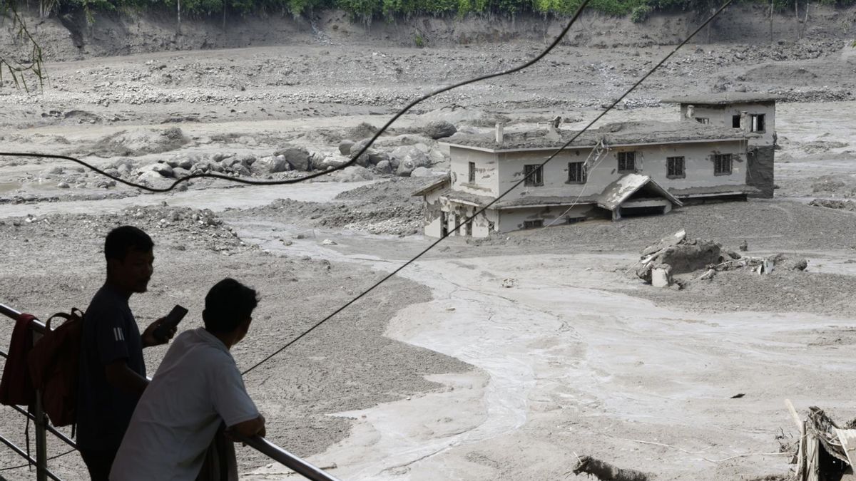 Varias personas observan cómo las aguas de la inundación arrasan Trishuli Bazar tras una crecida repentina, en el distrito de Nuwakot, Nepal.