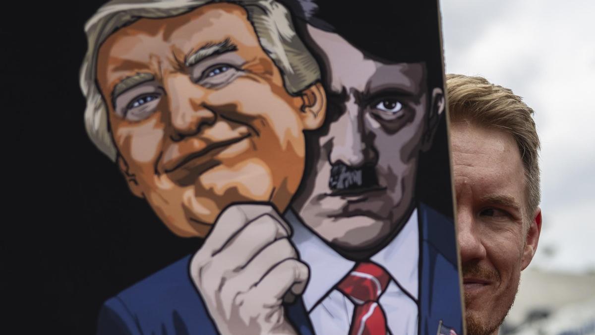 Un manifestante, representante de sindicatos locales y grupos de la sociedad civil, sostiene una pancarta con la imagen del presidente estadounidense Donald Trump y de Adolf Hitler.