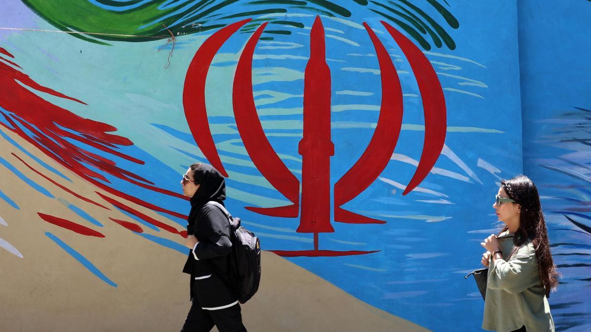 Ciudadanos iraníes pasan junto a un mural con la bandera nacional de Irán en una calle de Teherán, Irán.