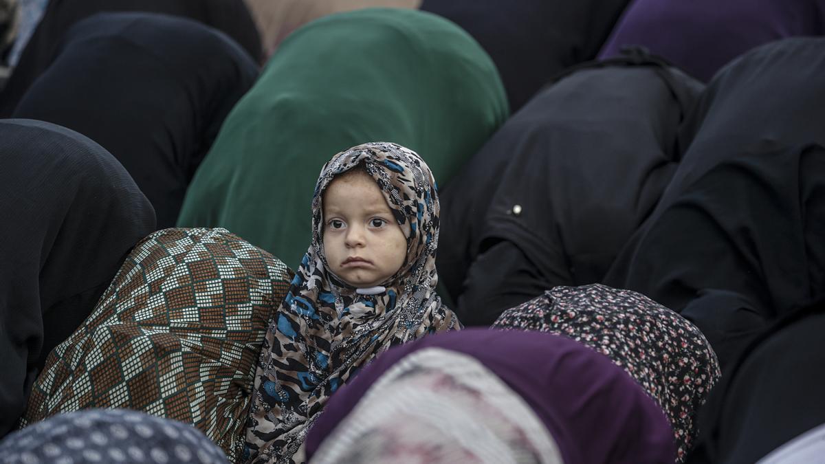 Una niña permanece de pie mientras sus familiares rezan durante la festividad musulmana del Eid al-Adha (Día del Sacrificio o del Cordero) en la ciudad de Gaza, Palestina este viernes.
