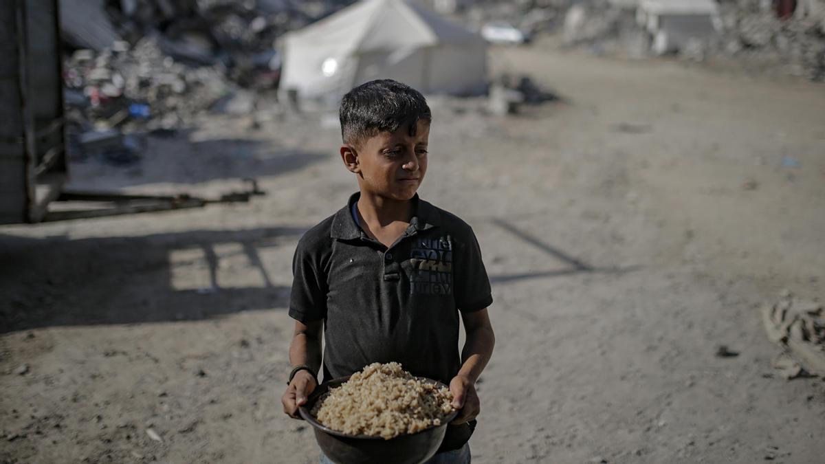 Un niño palestino lleva una olla de arroz después de recibir comida de un comedor social, en la ciudad de Gaza, el 23 de octubre de 2025.