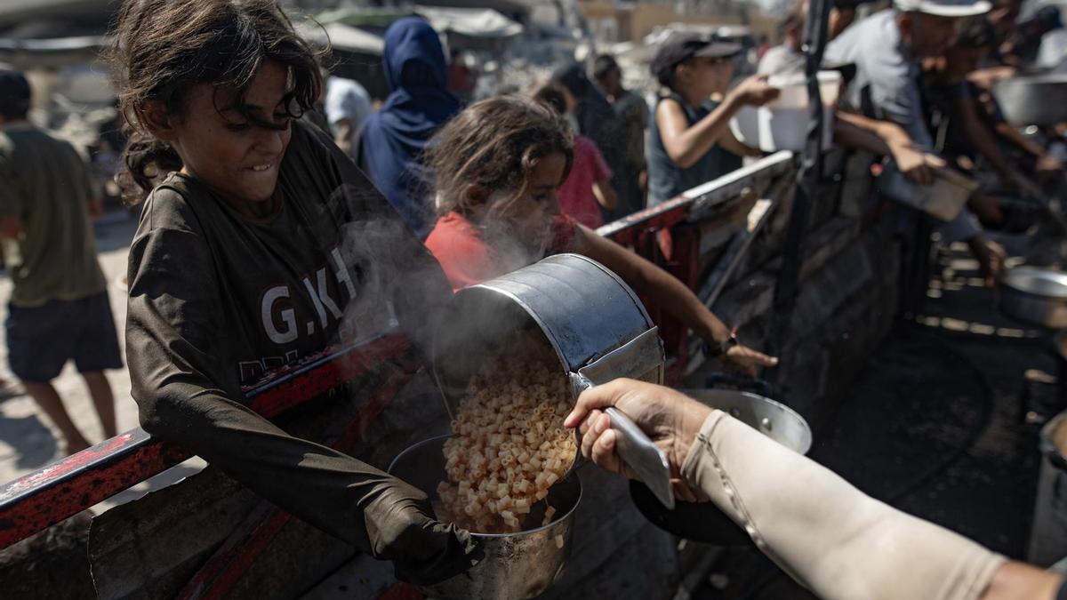 Niños palestinos sostienen ollas mientras hacen fila para recibir comida.