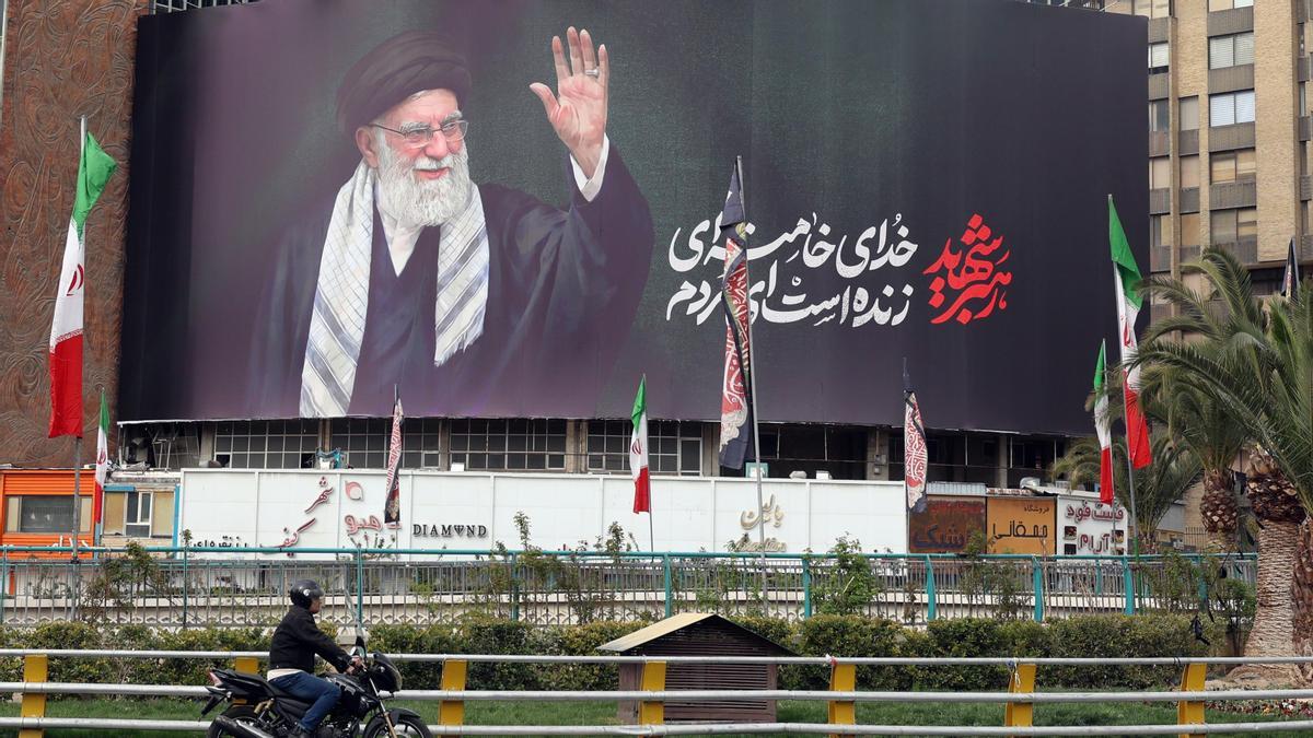 Los iraníes pasan en coche junto a una valla publicitaria del líder supremo iraní, el ayatolá Alí Jamenei, en Teherán.