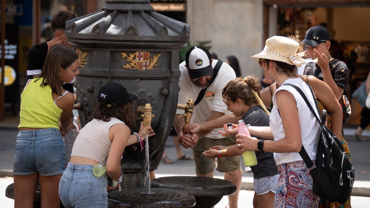 Varias personas se refrescan y rellenan sus botellas de agua en la fuente de Canaletas,  en Barcelona.