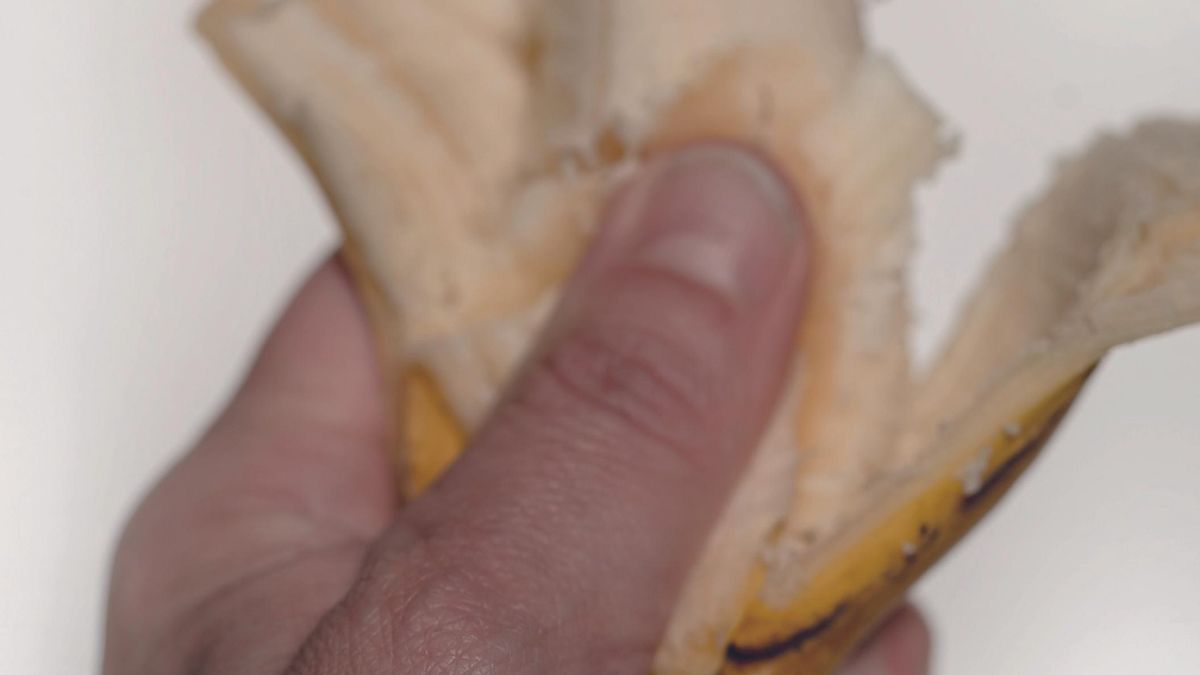Una foto de un plátano aplastado por una mano masculina.