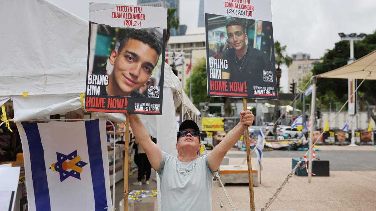 Un hombre sostiene fotos del soldado israelí-estadounidense Edan Alexander mientras la gente se reúne para ver en directo su liberación, frente a la base militar de Kirya en Tel Aviv.