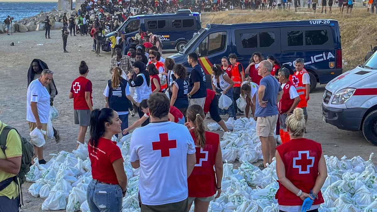 Miembros de la Cruz Roja de Ceuta reparten bolsas de comida a personas migrantes, en la playa ‘El Trampolín’ de Ceuta.