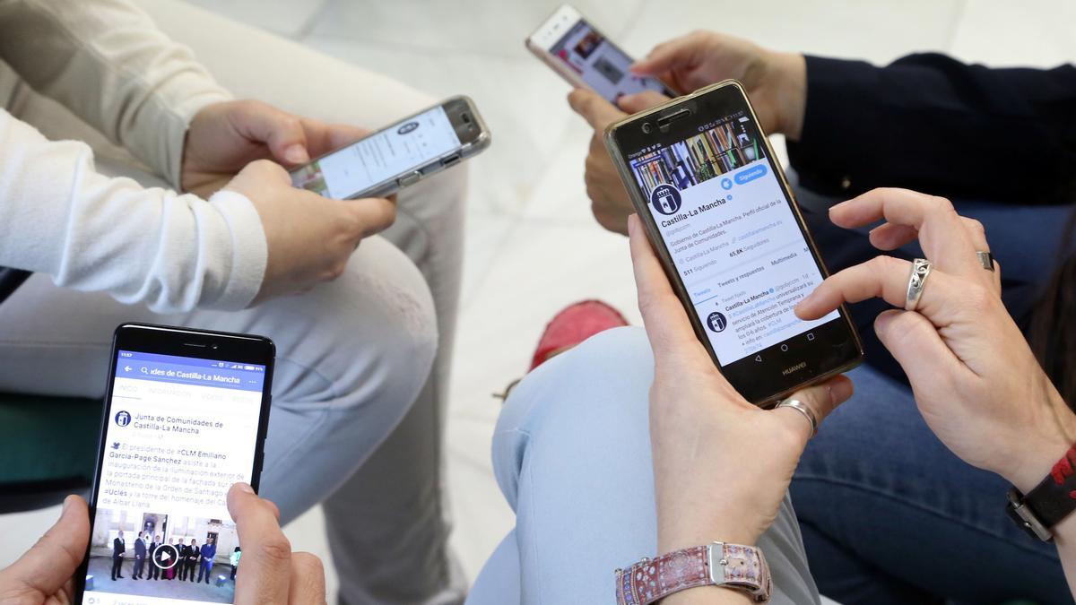 Archivo - Varios jóvenes observan sus redes sociales en sus móviles.