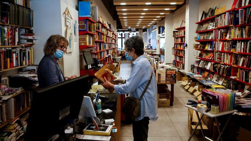 El librero Eric del Arco, de la histórica librería Documenta de Barcelona, atiende a una clienta al inicio de la fase 0 de la desescalada por la crisis del coronavirus.