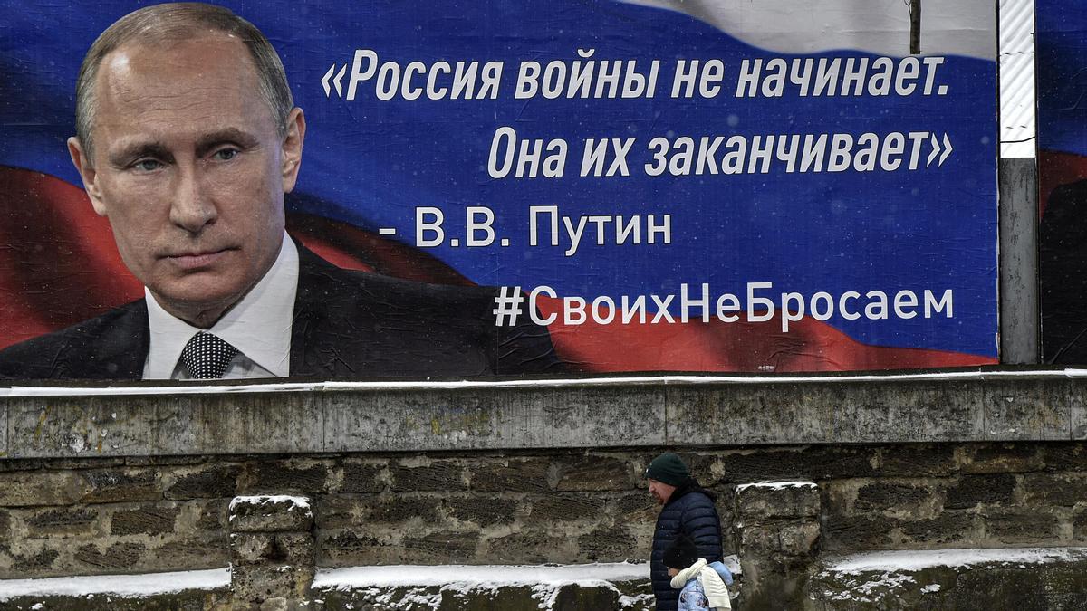 Un grupo de personas pasa junto a un cartel con la imagen del presidente ruso Vladimir Putin y lemas que dicen 'Rusia no empieza las guerras, las termina' en una calle de Simferopol, Crimea.
