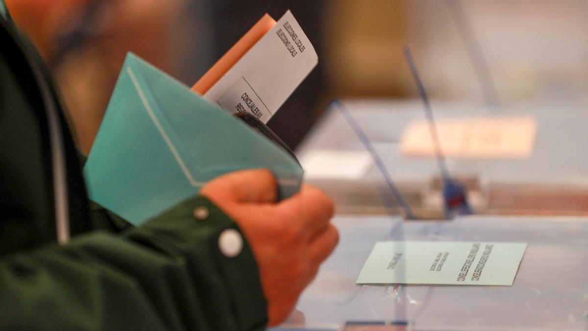 Una persona sostiene papeletas electorales frente a las urnas