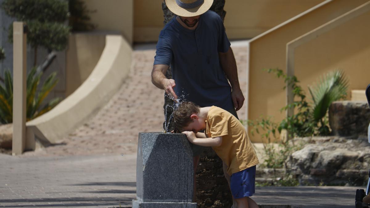 Un hombre refresca a su hijo en una fuente de una calle céntrica de Córdoba.