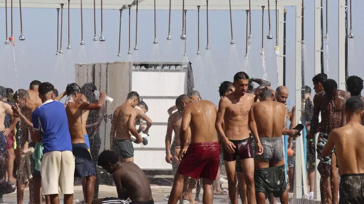 Migrantes se duchan en la playa de El Trampolín de Ceuta este sábado.