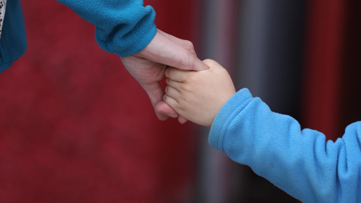 Un niño camina de la mano de un adulto.