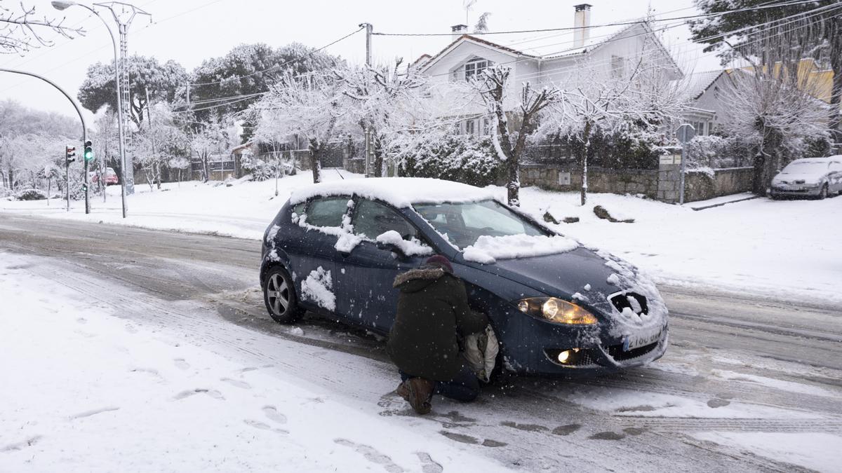 Un hombre pone las fundas a las ruedas de su coche para poder circular en una carretera en Alpedrete, este miércoles, en el que la borrasca Kristin deja nieve en la región de Madrid.