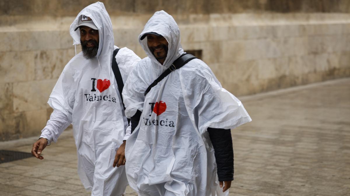Dos personas pasean bajo la lluvia protegidos con chubasqueros en Valencia.