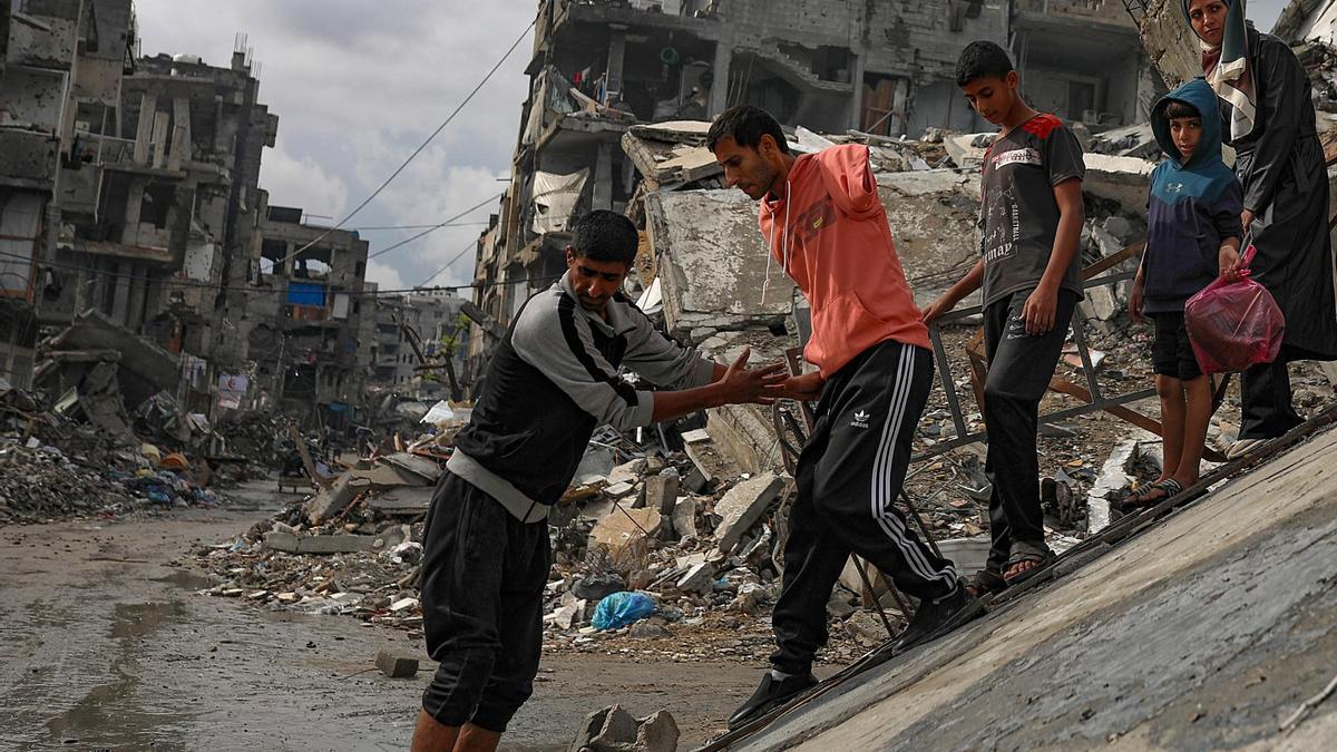 Palestinos caminan entre las ruinas de casas destruidas en el barrio de Sheikh Radwan durante un día lluvioso en la ciudad de Gaza, el 14 de noviembre de 2025.
