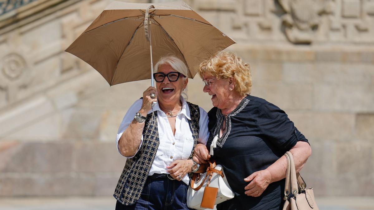 Dos mujeres usan un paraguas para protegerse del sol este lunes en la plaza del Obradoiro, en Santiago de Compostela.