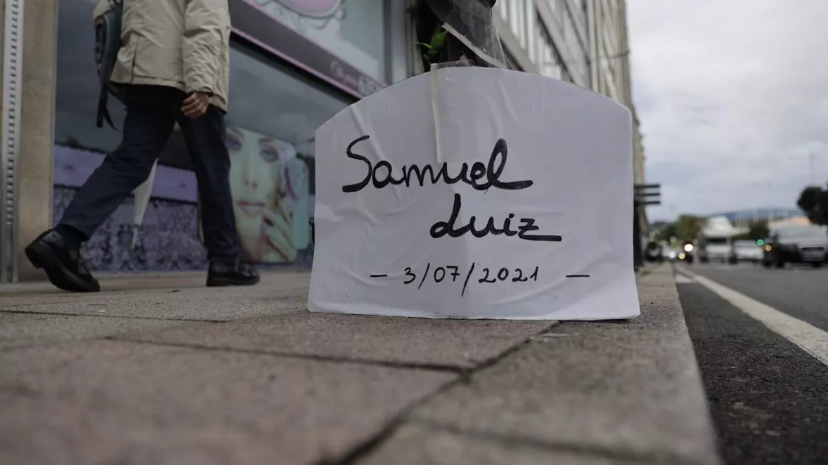 Un cartel con el nombre de Samuel Luiz situado en el lugar donde el joven recibió los golpes fatales que acabaron con su vida.