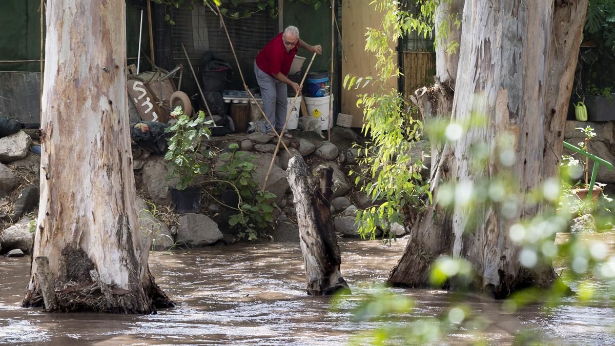 Un vecino del barranco de Arguinegín trata de proteger su vivienda ante la crecida del caudal del barranco, en Canarias.
