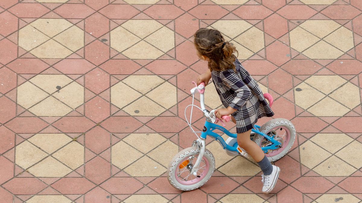 Una niña juega con su bicicleta en una plaza.