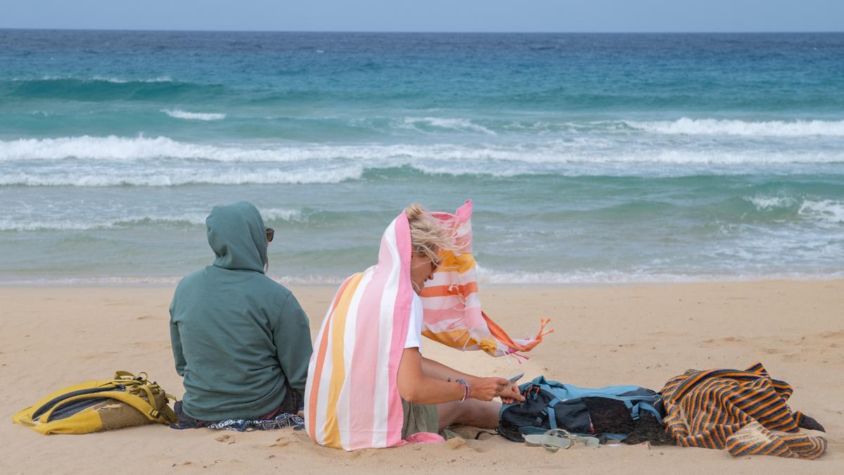 Dos personas se cubren del viento este domingo, en las playas de Corralejo, en el municipio de La Oliva (Fuerteventura).