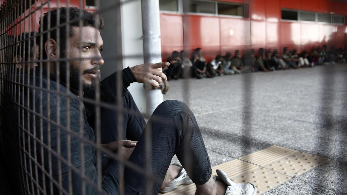 Refugiados y migrantes se sientan frente a la Autoridad Portuaria Griega tras ser transportados en pequeñas lanchas desde un granelero, en el puerto de Lavrio.