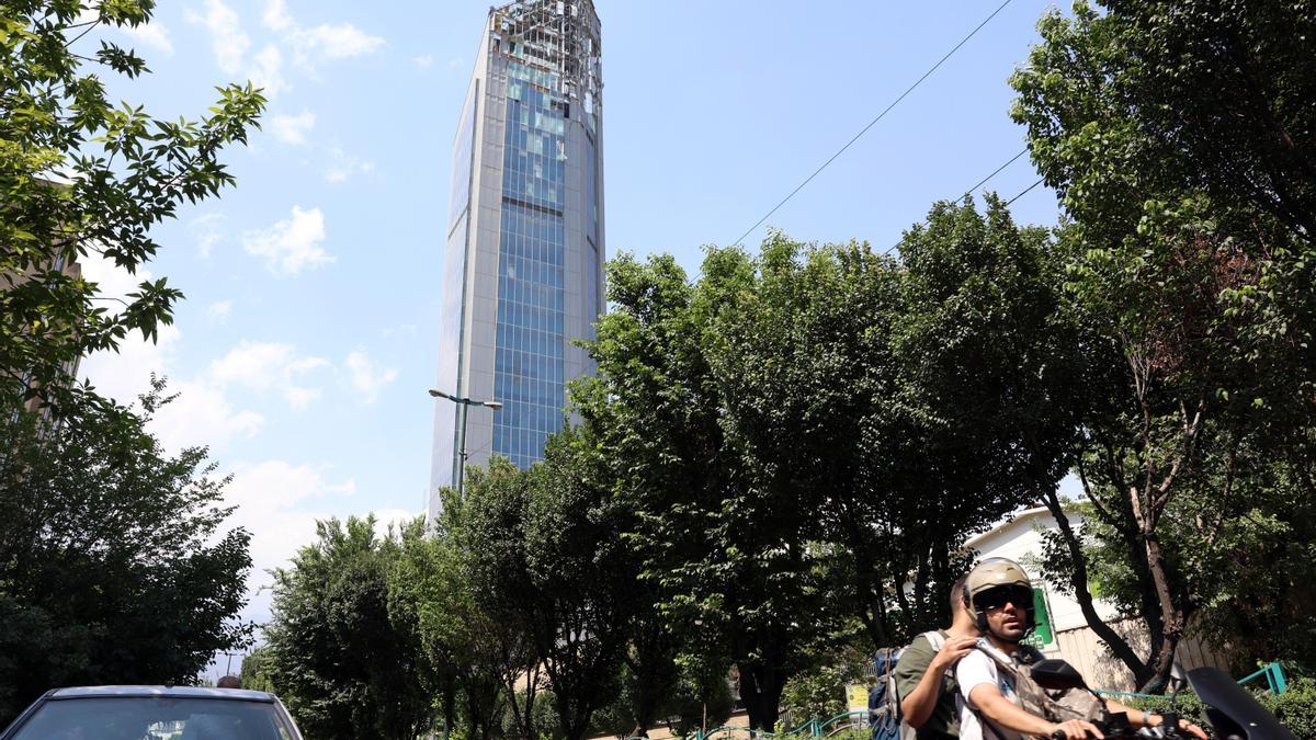 Personas pasan junto a un rascacielos dañado por ataques aéreos israelíes, al norte de Teherán, Irán.